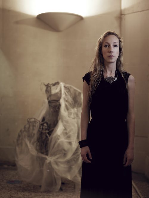 Image info: Iris van Herpen, courtesy Jean Baptiste Mondino and Iris van Herpen. Artist with dress exhibit in background.