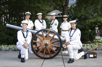 Canadian Navy Unit in white uniform smiles for camera beside cannon.