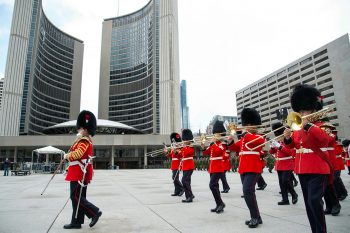 Trumpeters in red military coats march on Nathan Philips Square. 