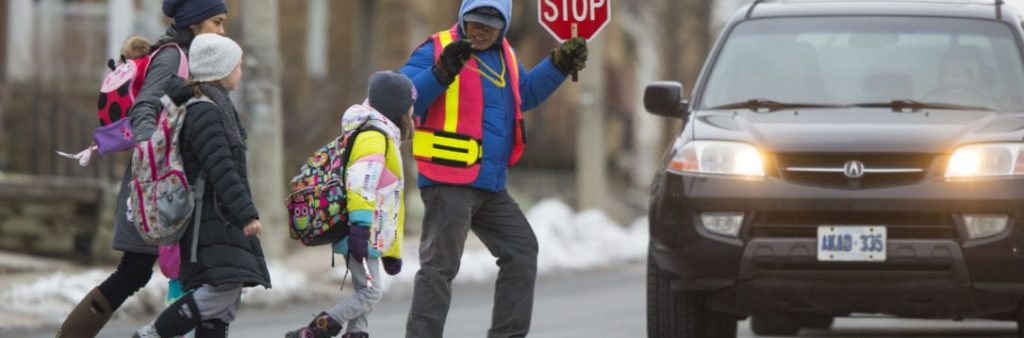 Image of a school crossing guard helping 3 children cross the street safety