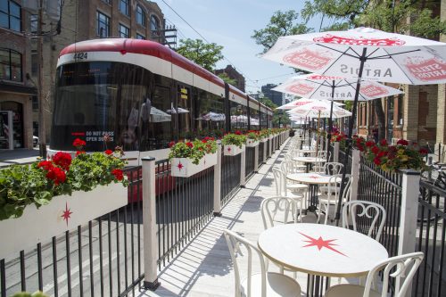 Streetcar passing by curb lane cafe with seating and umbrellas