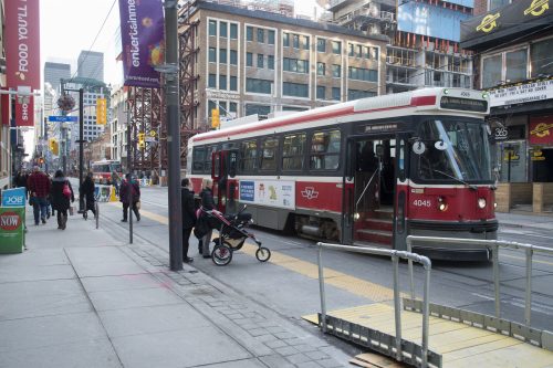 Streetcar stopped at TTC stop with accessibility ramp and people waiting to get on streetcar