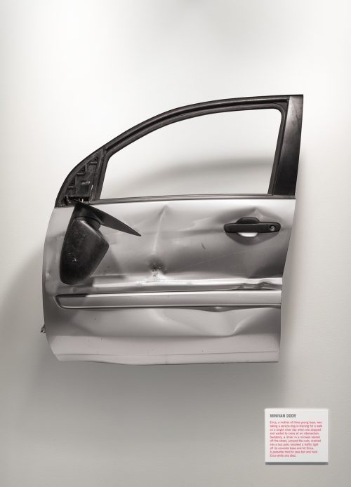 A dented minivan door is suspended in mid-air like an exhibit in an art gallery.