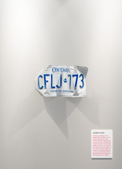 A licence plate is crushed up and mounted on the wall like an exhibit in an art gallery.