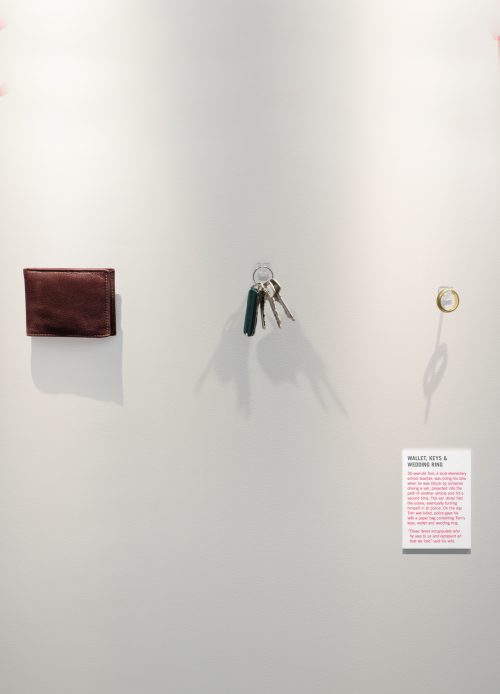 A wallet, a set of keys and a man’s wedding ring are mounted on the wall like an exhibit in an art gallery.