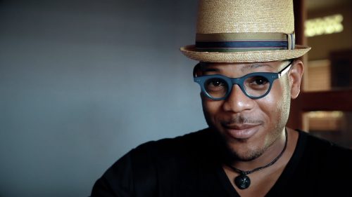 Image info: Etienne Charles. Close up of man with hat and glasses