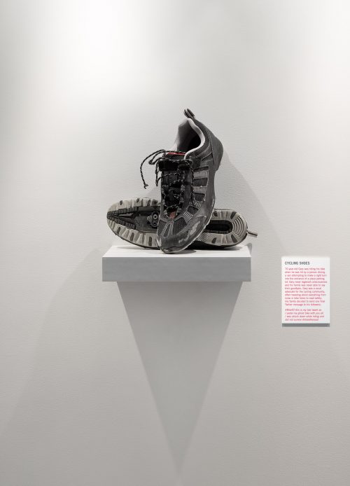 A pair of cycling shoes sit on a small shelf like an exhibit in an art gallery.