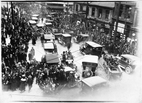 People and cars on street celebrating Armistce Day