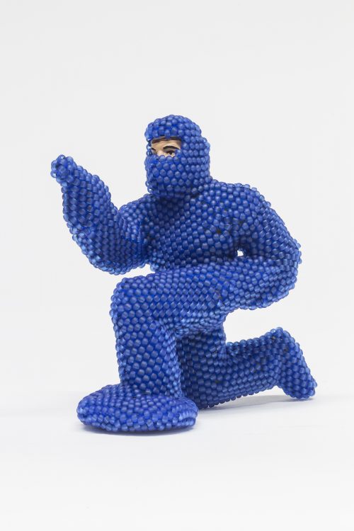 Image info: Bev Koski, Ottawa #1 (2014), 8 x 4.5 x 8.5cm. human figure in blue, bubble wrap, full body suit. crouching, pointing.