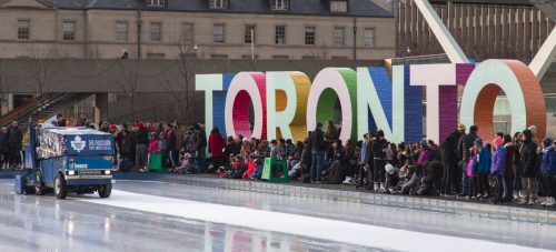 Zamboni on Nathan Phillips Square ice rink. Toronto sign. people waiting on side to skate.