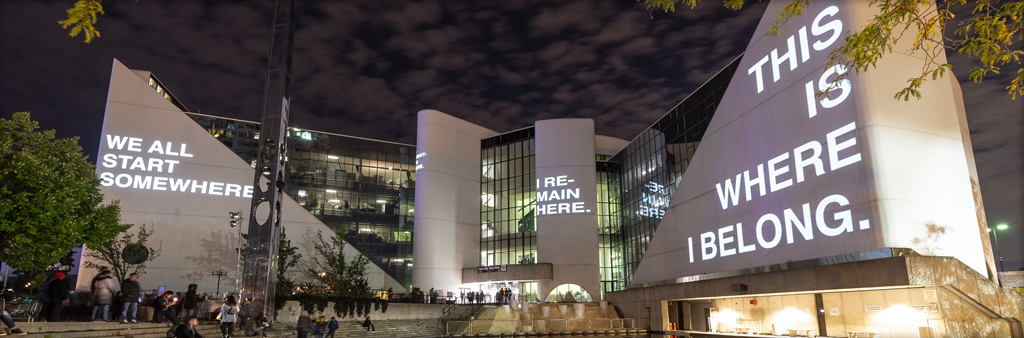 Nuit Blanche 2018 art exhibit called Scarborough Everything I wanted to tell you by Hiba Abdallah shows a projection of the words "We All Start Somewhere. I Remain Here. This is Where I Belong." on to the Scarborough Civic Centre