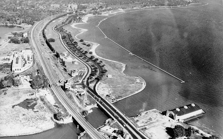 An old photograph from the late 1950s shows an aerial view of the newly build Gardiner Expressway snaking eastbound from approximately Sunnyside Pavillion to Toronto's downtown.