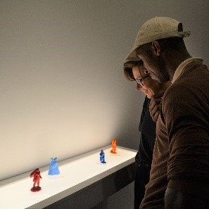 People looking down at textile display on white shelf, lit from behind.