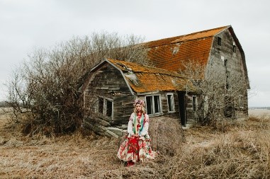 Photo info: Featured, Lianna Makuch. Photo credit: Mat Simpson. Dilapidated barn in background. woman in colourful dress in foreground.