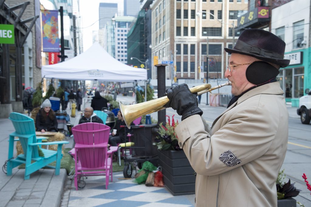 Elderly man playing trumpet in public space with seating and people in background