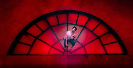 Performer on red stage. Black outline of a window - 1/2 circle. With bars.