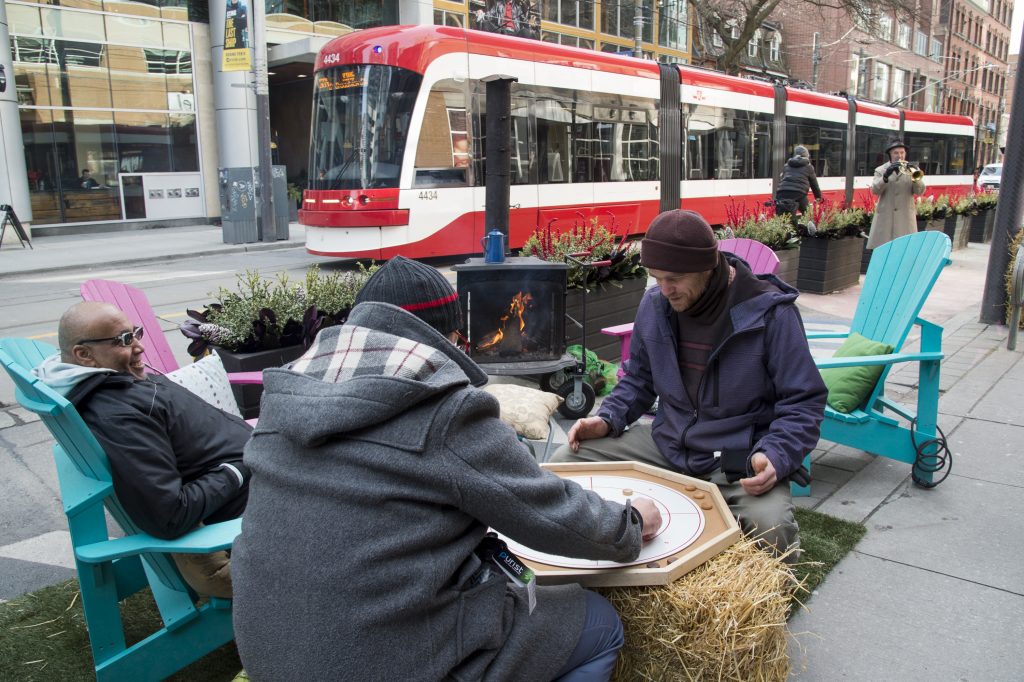3 men playing a board game on the curbside of king street with a streetcar in the background