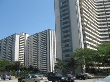Three apartment towers in the 280 Wellesley St. E. complex with cars parked outside on a sunny day.