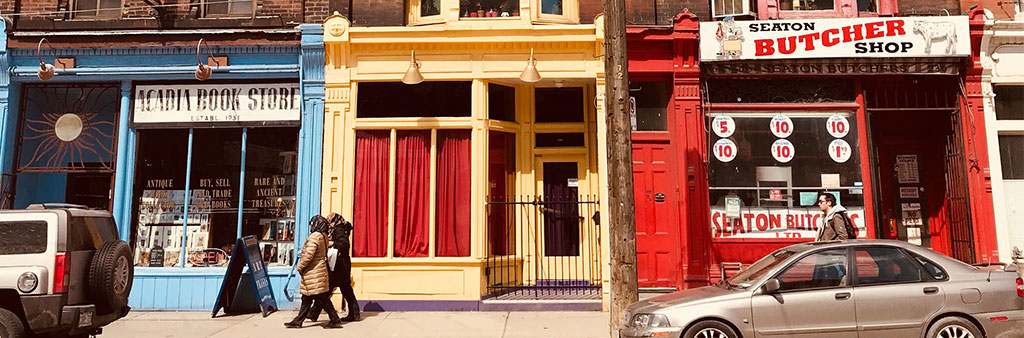 Three storefronts in Toronto with people walking on the sidewalk.