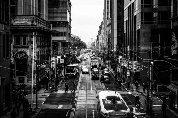 Black and white photograph of a busy city street filled with street cars, cars, and pedestrians.