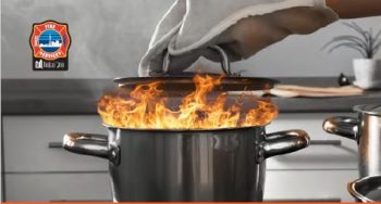 Hand wearing oven mitt putting a lid on a flaming pot