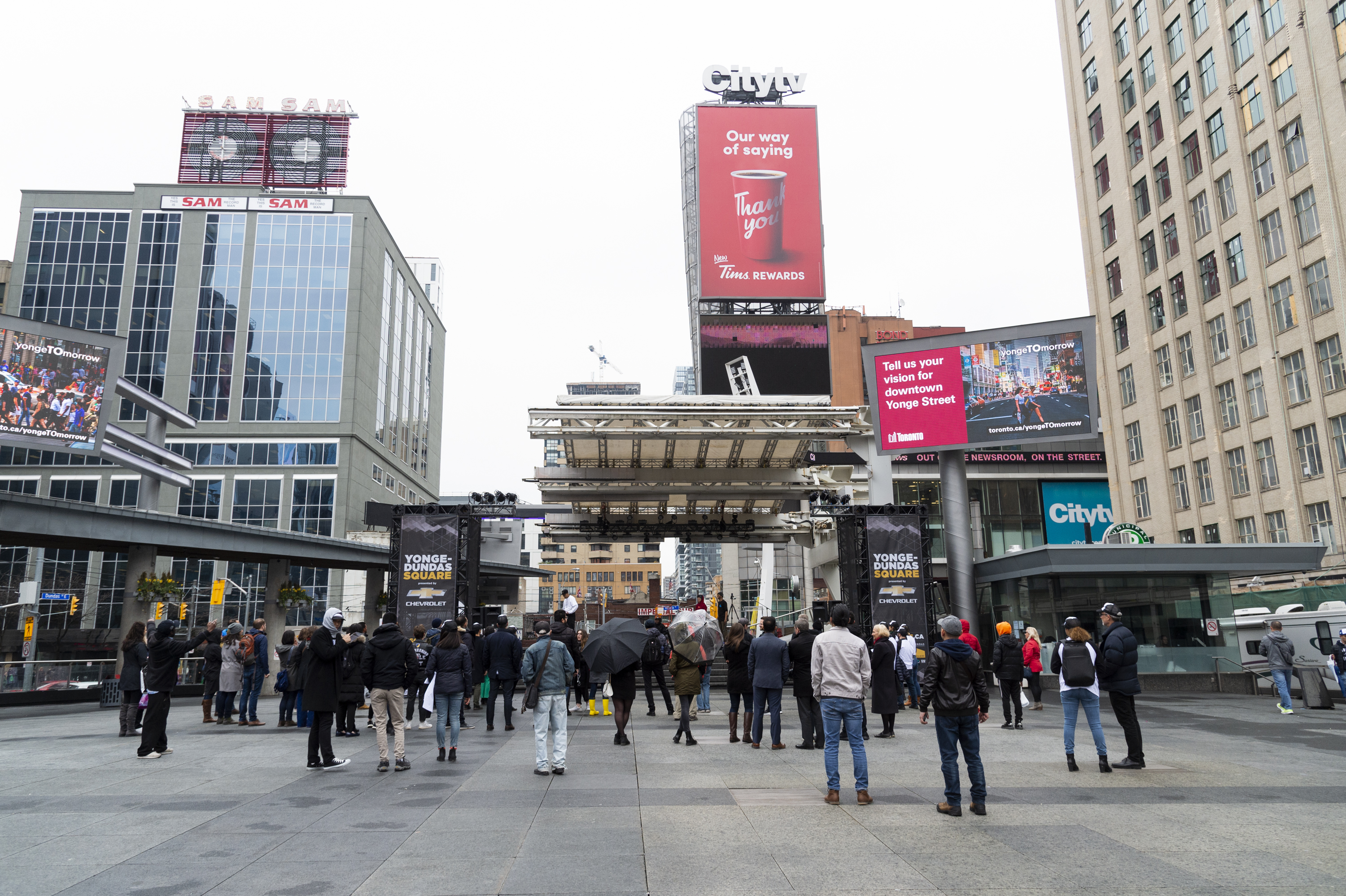 Yonge and Dundas square at the launch event, please standing looking at the stage during the presentation on a rainy day