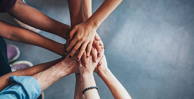 five people placing their hands on top of each other to signify teamwork.