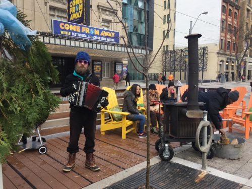 Man playing accordion with people sitting around wood stove