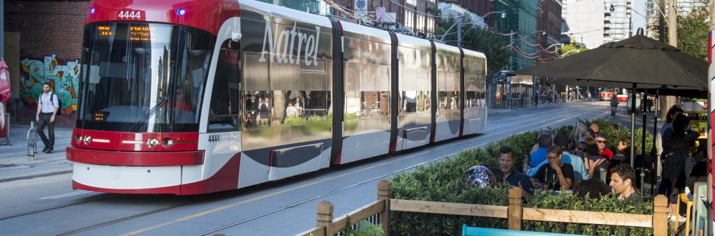 Streetcar moving westbound passing patio and public seating area