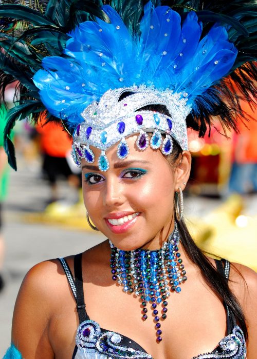 Woman facing camera, in blue headdress, colourful costume.