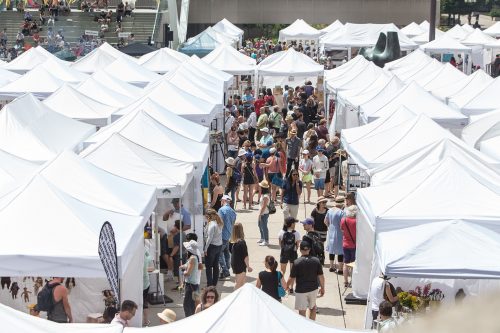 White tents, many people attending outdoor art fair. Image taken from above.