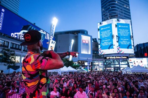 Man performing in front of crowd at Yonge Dundas Square - Eaton Centre in background, at dusk.