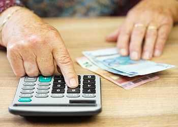 A person's hand at a desk with a calculator and cash.