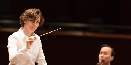 Image info: Tania Miller. Conductor, with musician in background.