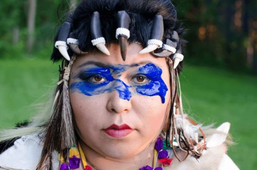 Image info: Jaene Castrillon - A Celebration of Darkness, Photo: courtesy of Jackie Lozer . Woman with blue paint around eyes, claws around forehead.
