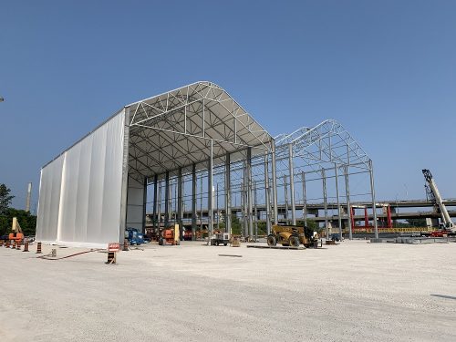 Image of Gardiner Expressway Strategic Rehabilitation, Jarvis to Cherry fabrication site located on lands near Lakeshore Blvd E and Cherry St. Image features two large tent structures, one with a canvas cover and the other just a metal frame with the Gardiner Expressway in the background.