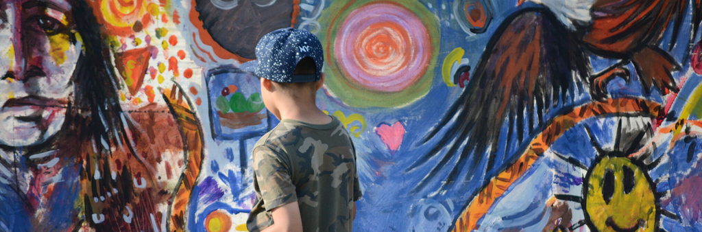 A kid with a baseball cap standing in front of a coulourful mural.