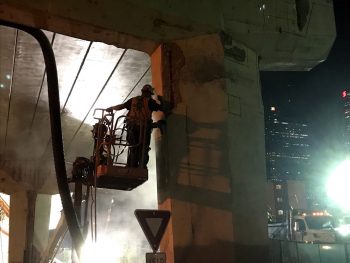 Image of a construction worker in a cherry picker chipping concrete under the bent of the Gardiner Expressway York-Bay-Yonge off-ramp