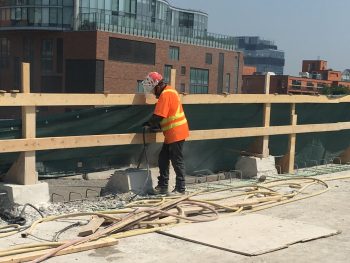 Image of construction worker chipping concrete on Gardiner Expressway York-Bay-Yonge off-ramp with safety netting and temporary wooden rails in the background