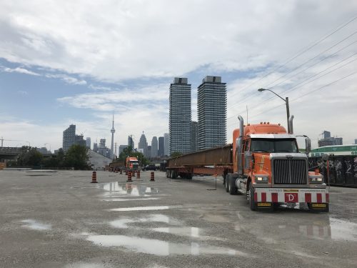 Image of trucks pulling up on the fabrication site with a steel girder