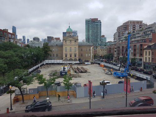 Construction progress at North St. Lawrence Market showing a crane, pipes and other construction equipment in dirt enclosure.