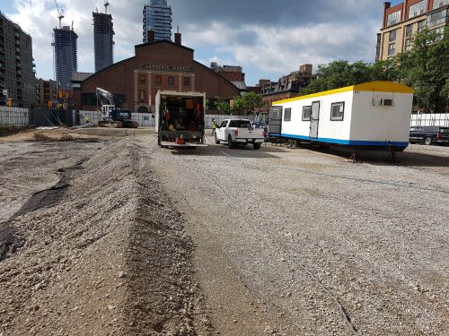 Construction progress at North St. Lawrence Market showing a pickup truck, moving truck and construction portable in dirt enclosure.