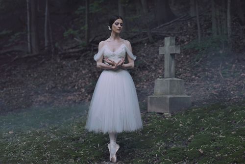 Image info: Giselle. Ballerina in long tutu, on pointe in cemetery, surrounded by fallen leaves, green grass.