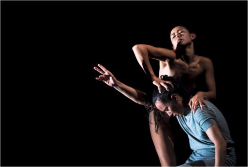 Image info: SPLIT. Credit: Gregory Lorenzutti. Two performers - one on knees reaching out. Other standing above, hands on head and shoulder of first performer.