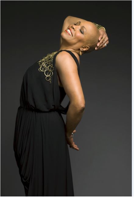 Image info: Dee Dee Bridgewater. Photo by-Mark-Higashino. Woman dressed in black, smiling, with arm holding head leaning back