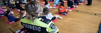 A paramedic leads children through a first aid course in a gymnasium