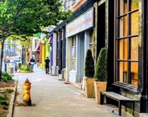 A typical retail oriented main street is shown with trees and shrubs in a short planter on the sidewalk in front of the retail units.