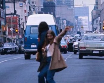 Photo of female standing and waving at the camera on Yonge Street with traffic in the background