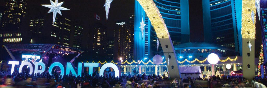 Nathan Phillips Square skating rink at night with Toronto Sign and arches glittering with lights.