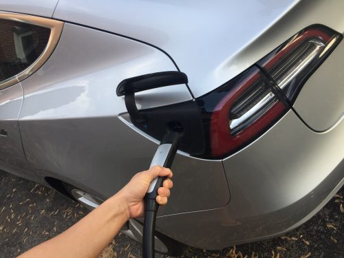 a hand holding an EV charger, plugged into a silver vehicle